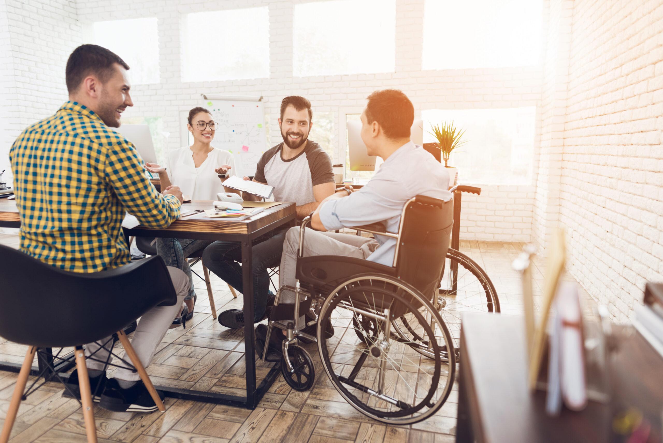 A man in a wheelchair communicates cheerfully with employees during a business meeting